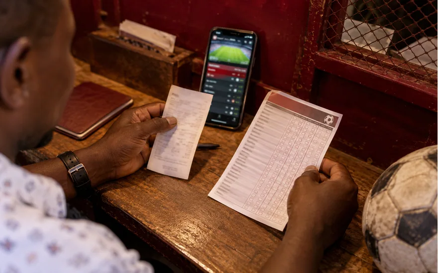 Adult comparing a receipt and printed record beside a phone and football