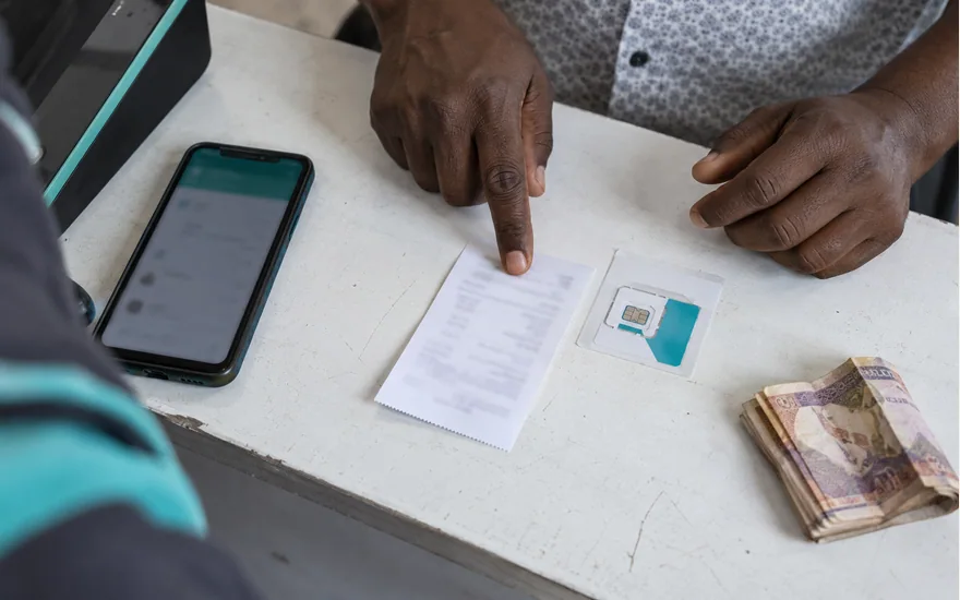 Hands pointing to a receipt beside a phone, SIM sleeve and folded notes