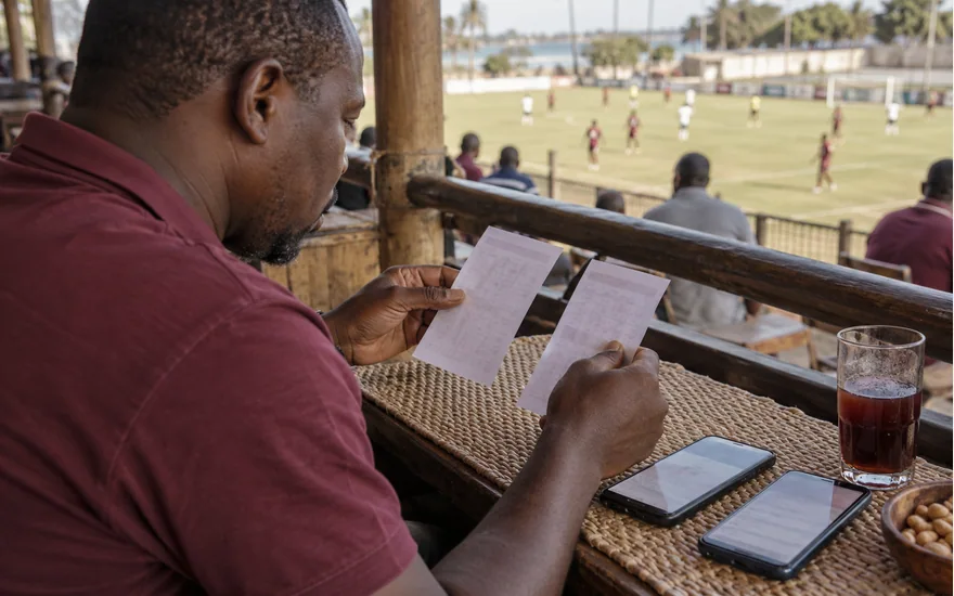 Adult reader comparing a sports coupon and phones overlooking a football ground