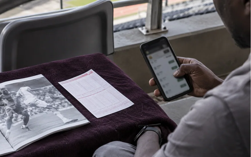 Phone and paper betting coupon beside a football programme on a plum covered seat