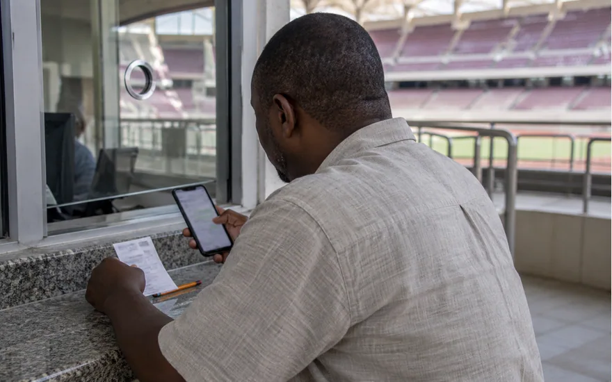 Man making notes beside a phone at a stadium service window