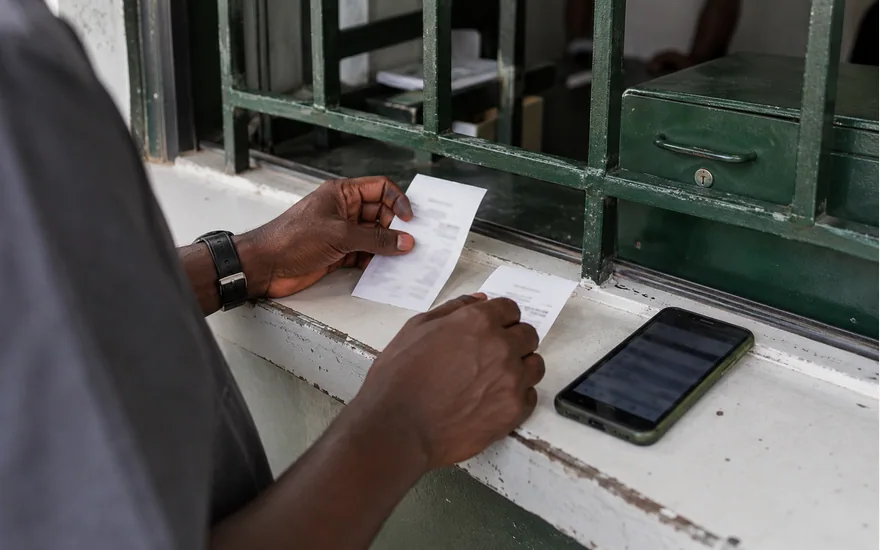 Hands organising receipts beside a phone at a green service window