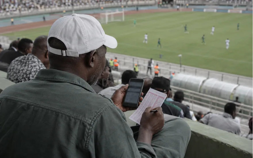 Adult spectator comparing a phone and ticket overlooking a football pitch
