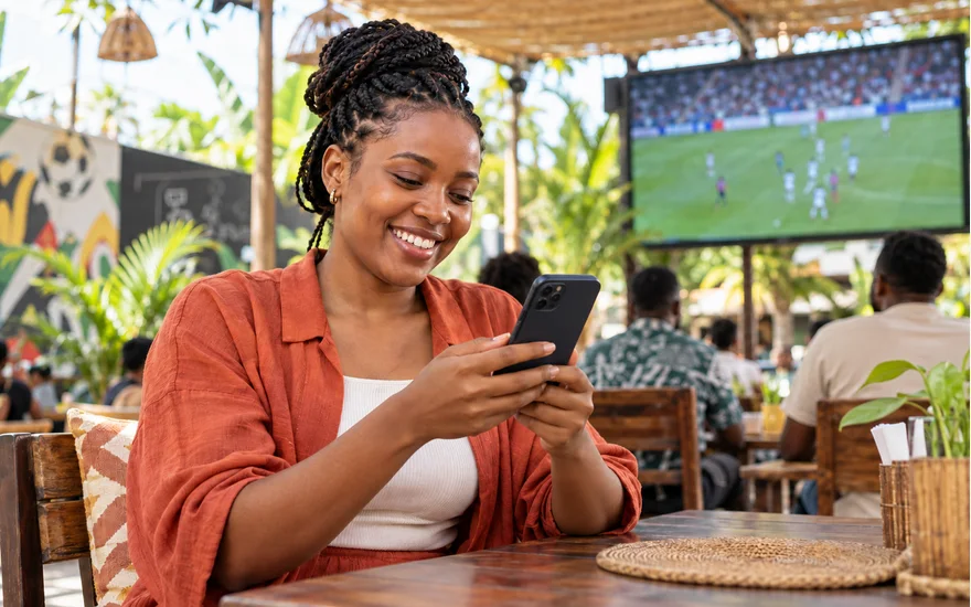 Smiling adult Tanzanian woman holding a phone in a bright football-viewing courtyard