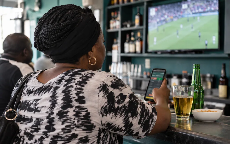 Woman checking a phone while a football broadcast plays at a cafe