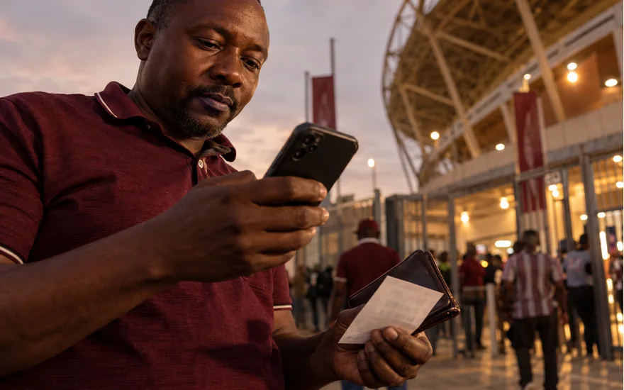 Man comparing a phone and small paper record outside a stadium