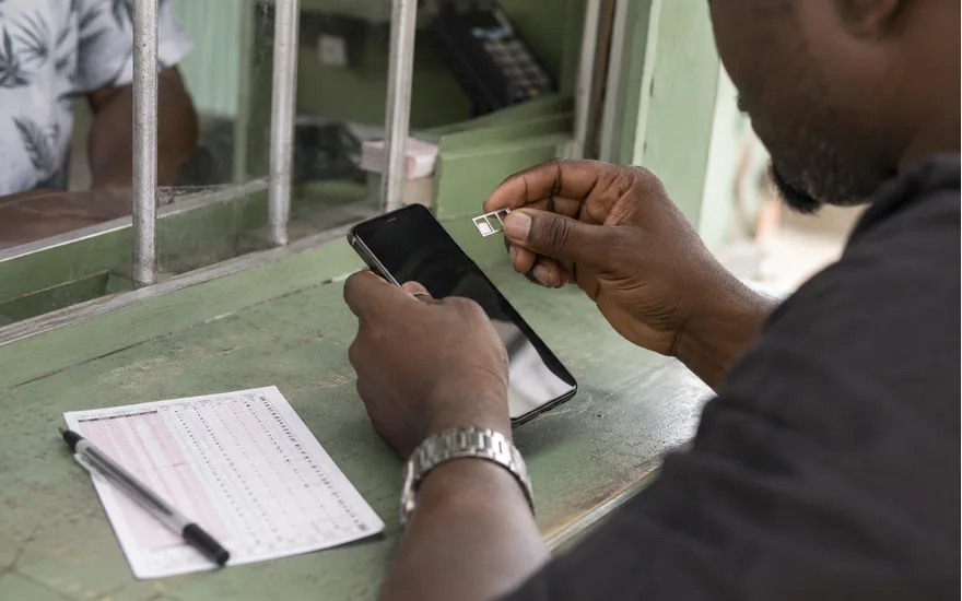 Hands handling a SIM tray beside a phone and paper form