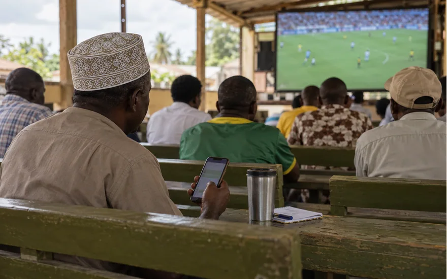 Adult checking a phone while football plays in a viewing shelter