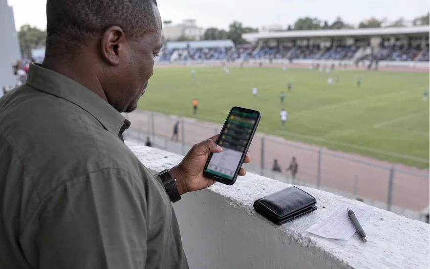 Man checking selections on a phone while overlooking a football pitch