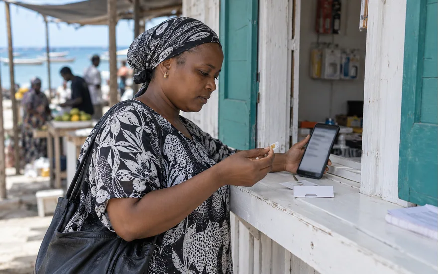 Mwanamke mtu mzima akikagua SIM kadi na simu katika kioski cha sokoni Tanzania