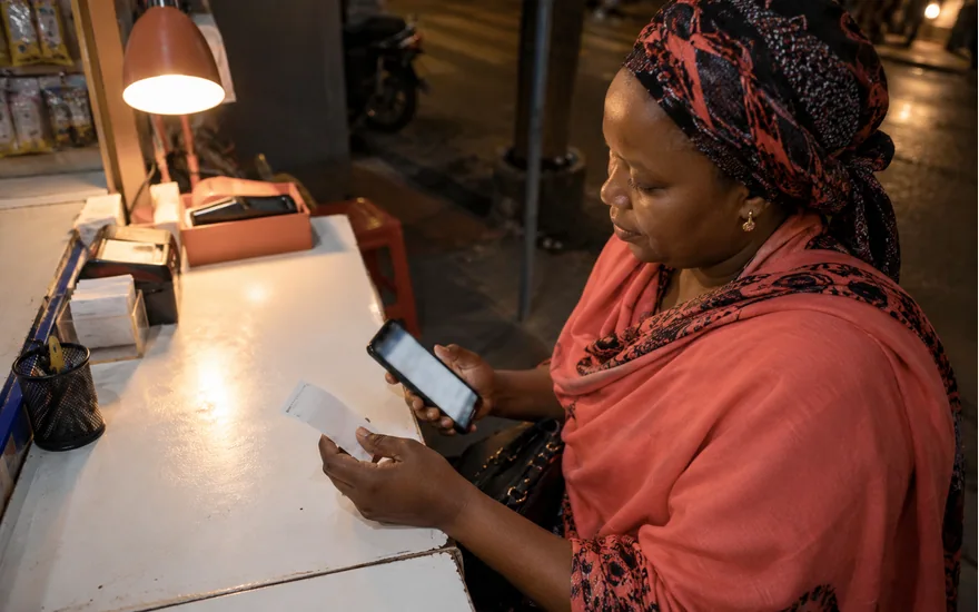 Woman comparing a phone and receipt at a lamp lit counter